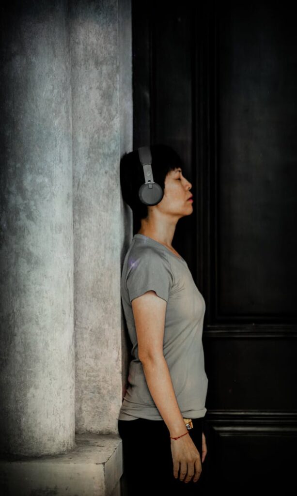 A woman in a gray shirt relaxes while listening to music with headphones, eyes closed.