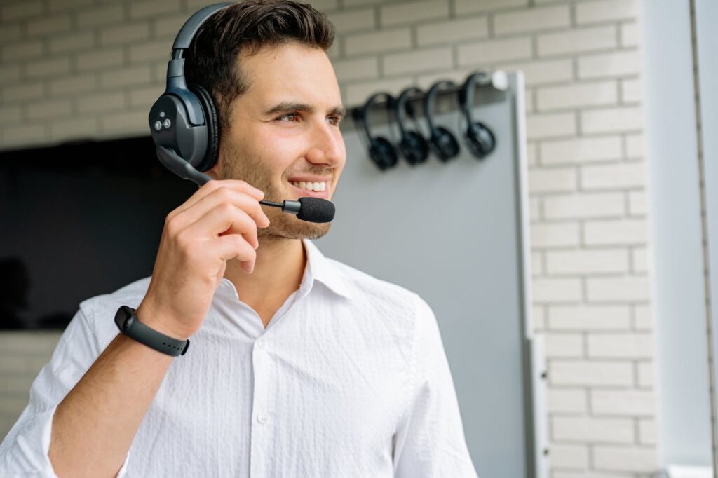 Young man with headphones and microphone standing indoors, smiling.