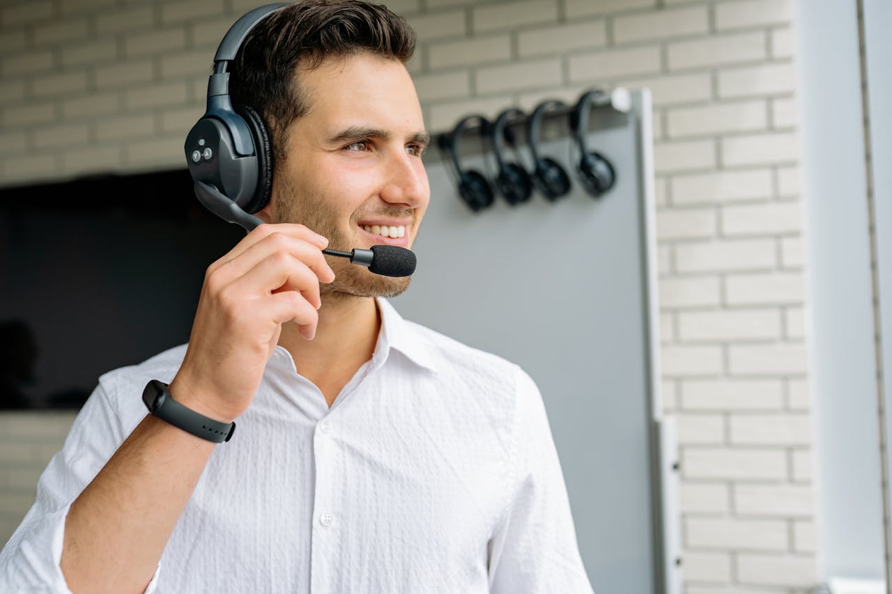 Young man with headphones and microphone standing indoors, smiling.